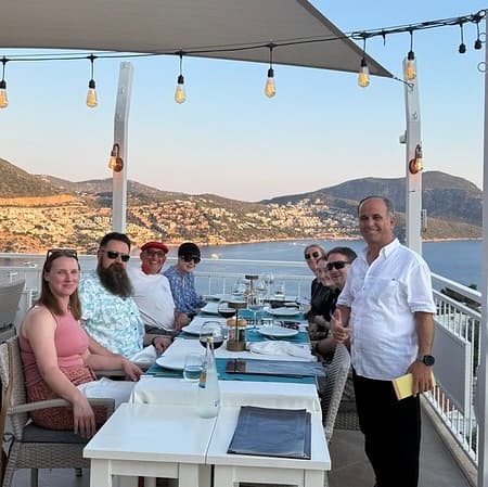 A group of friends sat around a table in a roof top restaurant with stunning view over Kalkan Bay