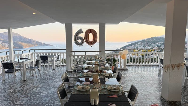 A restaurant terrace on top of a hotel, there is a huge 60 balloon in the background is Kalkan Bay