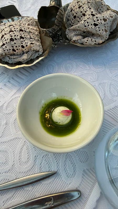 Butter in a bowl surrounded by green oil and bread wrapped in cloth